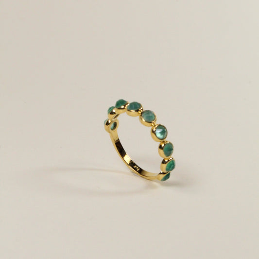 Gold ring with green gemstones on a light beige background