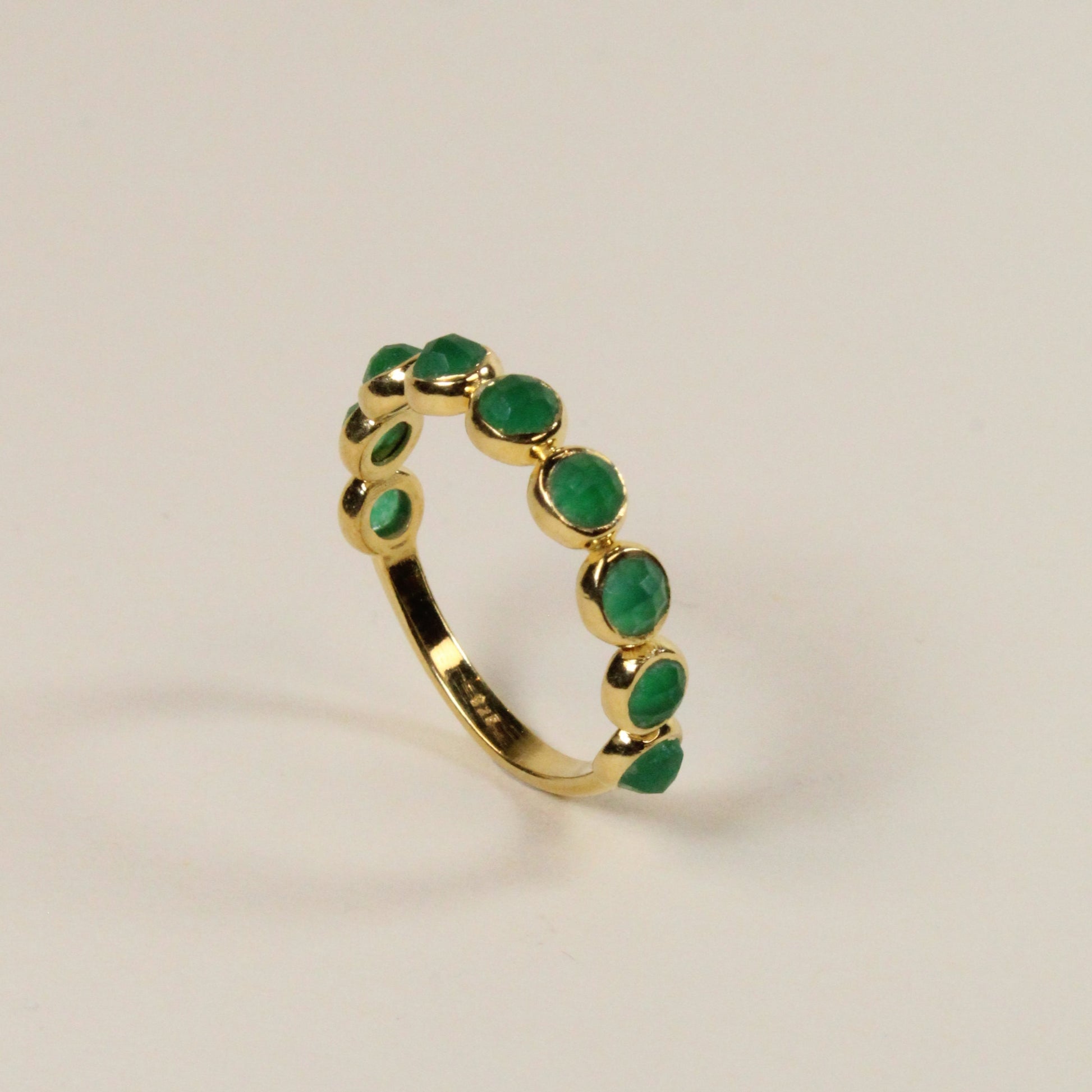 Gold ring with green gemstones on a light beige background
