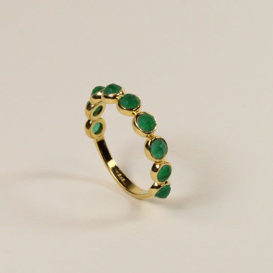 Gold ring with green gemstones on a light beige background