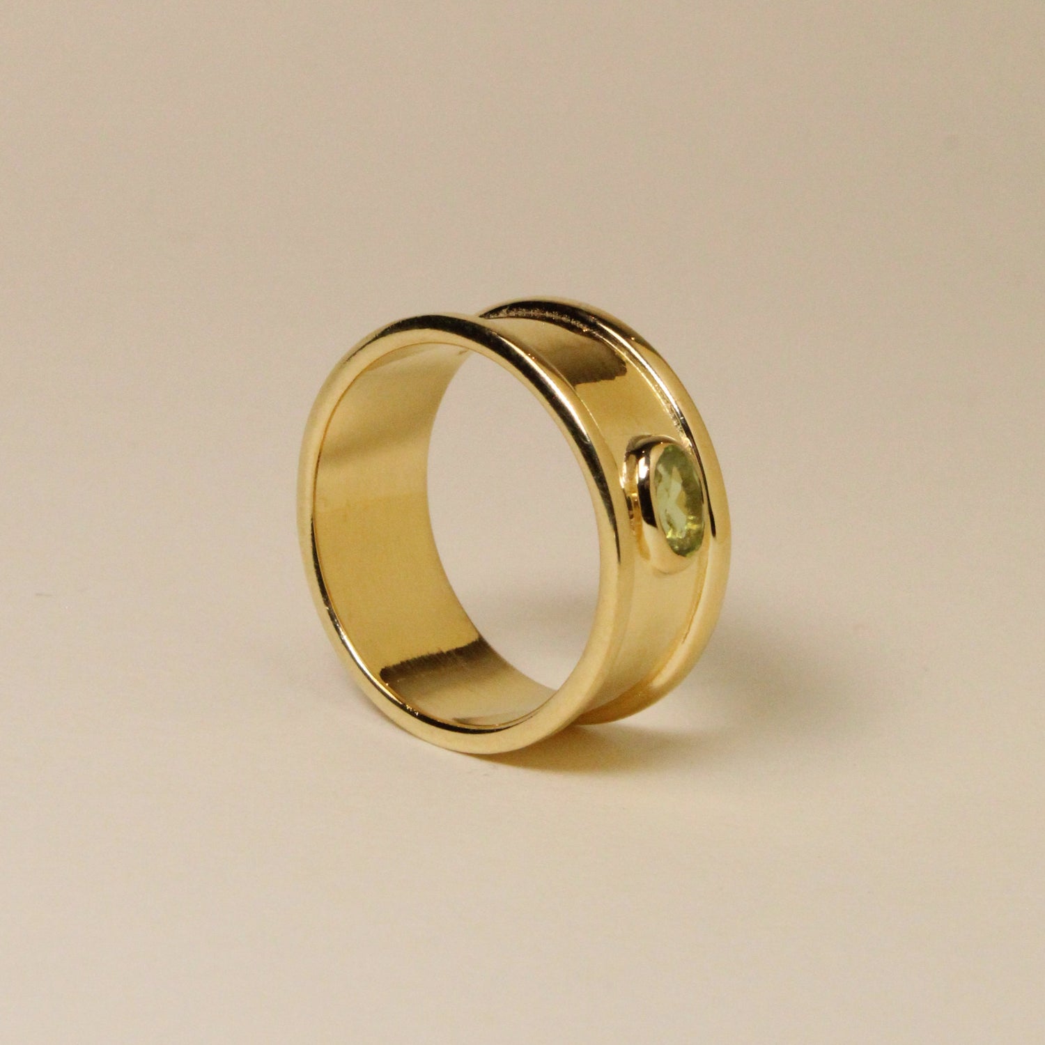 Gold ring with a green gemstone on a beige background